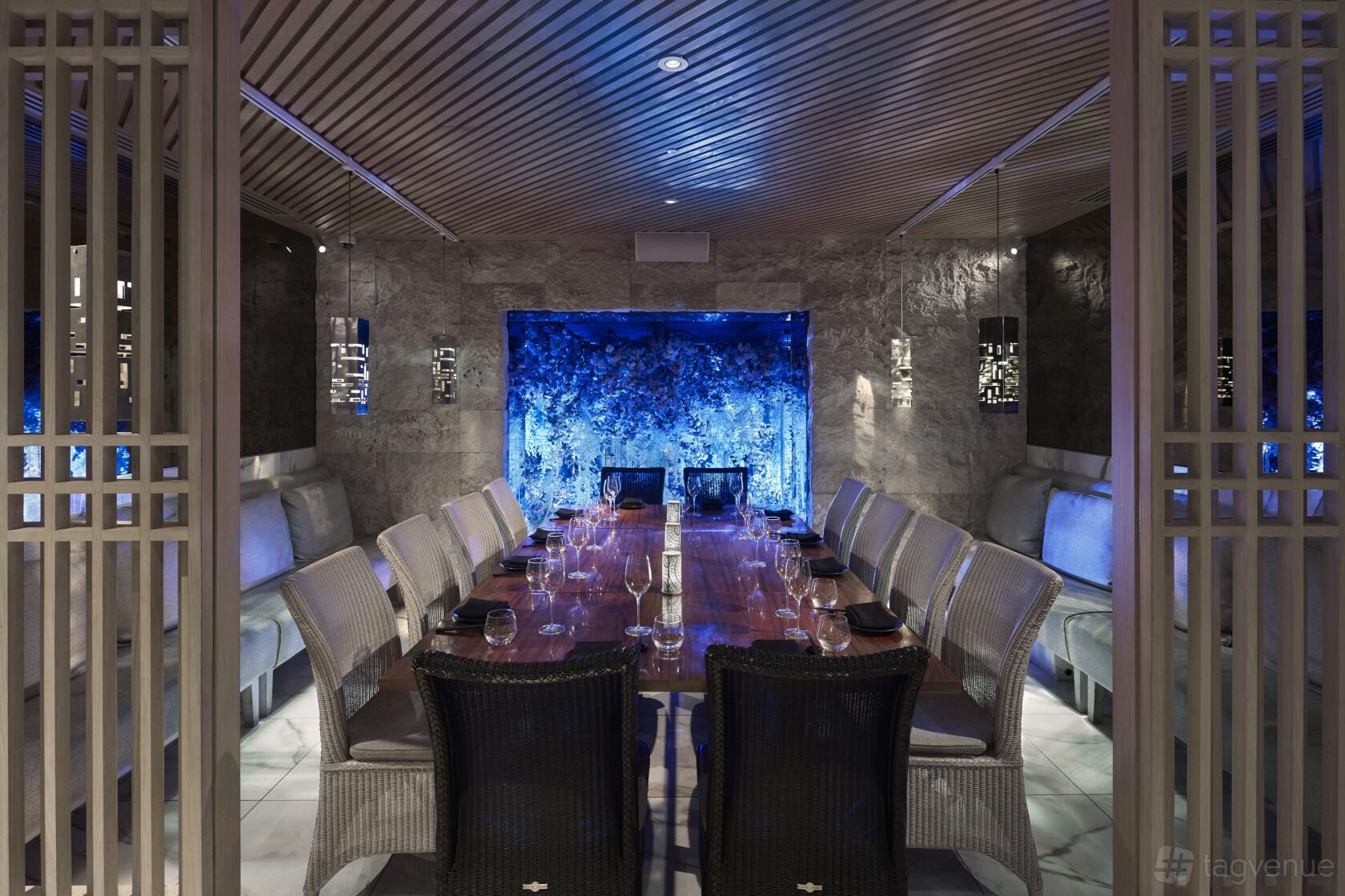 A private dining room with a long wooden table, plush seating, marble walls, and a blue illuminated feature at Tattu Birmingham.
