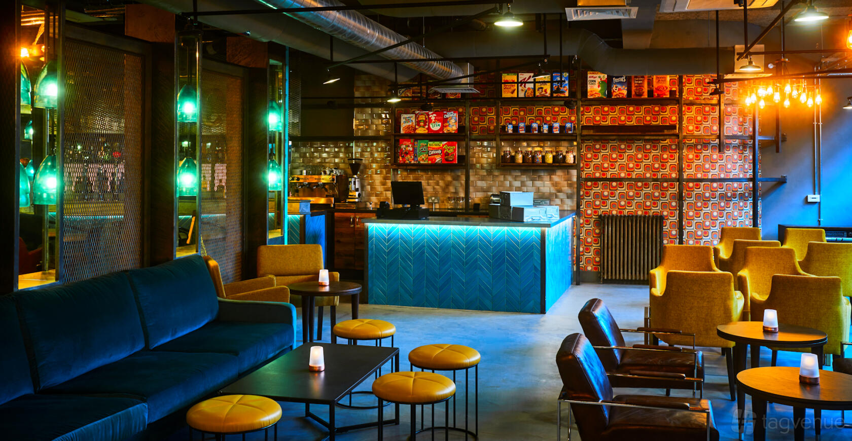 A coworking lounge with colorful armchairs, a blue-lit reception desk, and exposed brick walls at New Road Hotel.