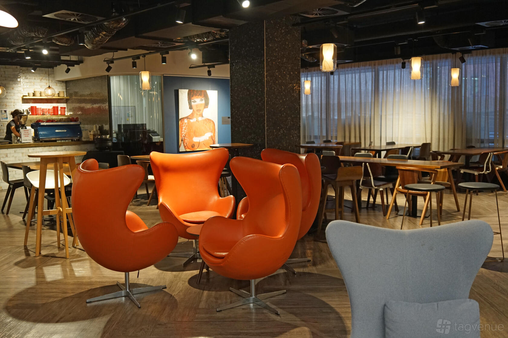 An event space with orange lounge chairs, round tables, wood flooring, and pendant lighting at Cliftons Sydney Spring St.