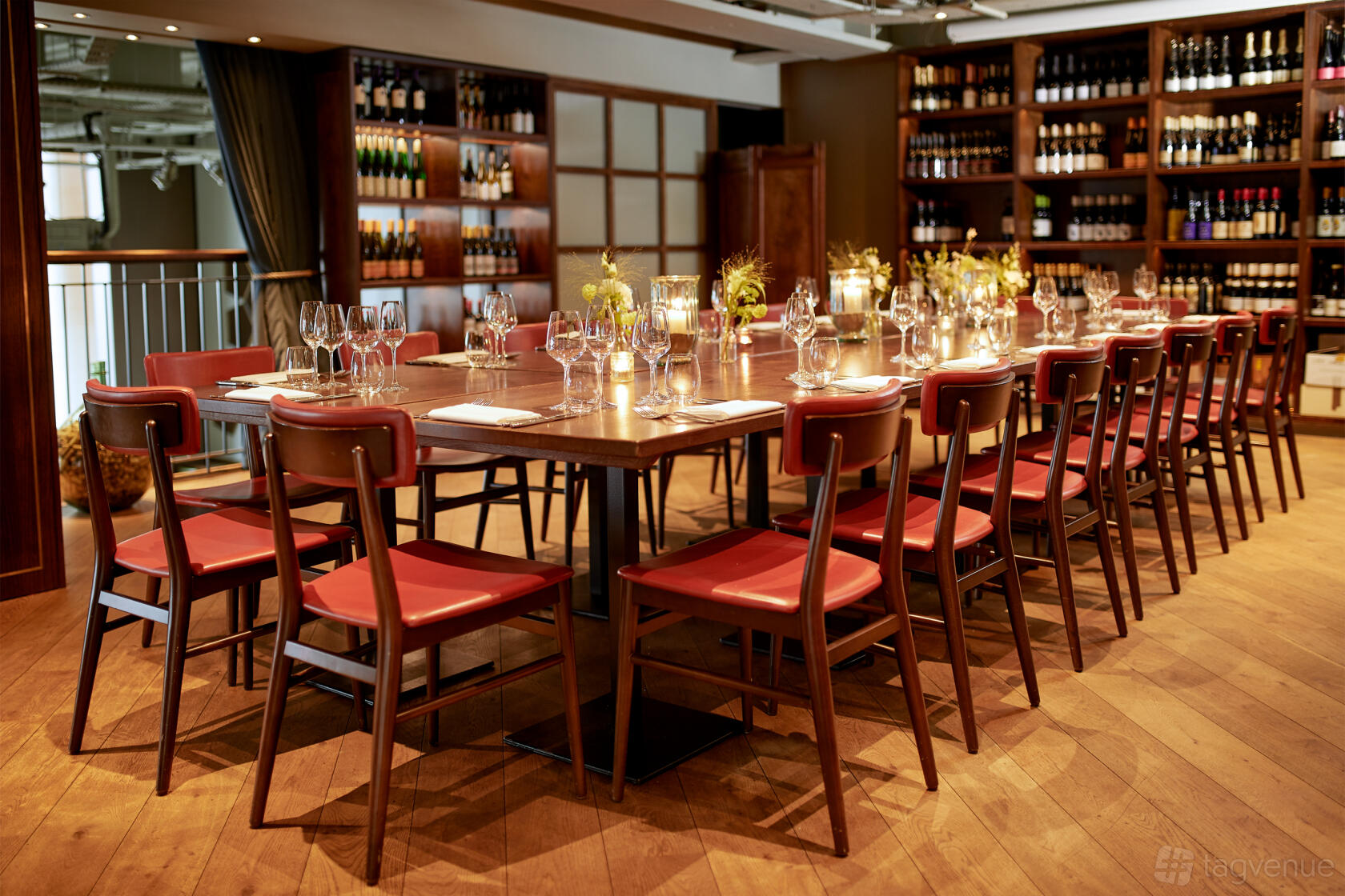 An event space with a long wooden table, red chairs, wine displays, and candlelit place settings at Vinoteca City.