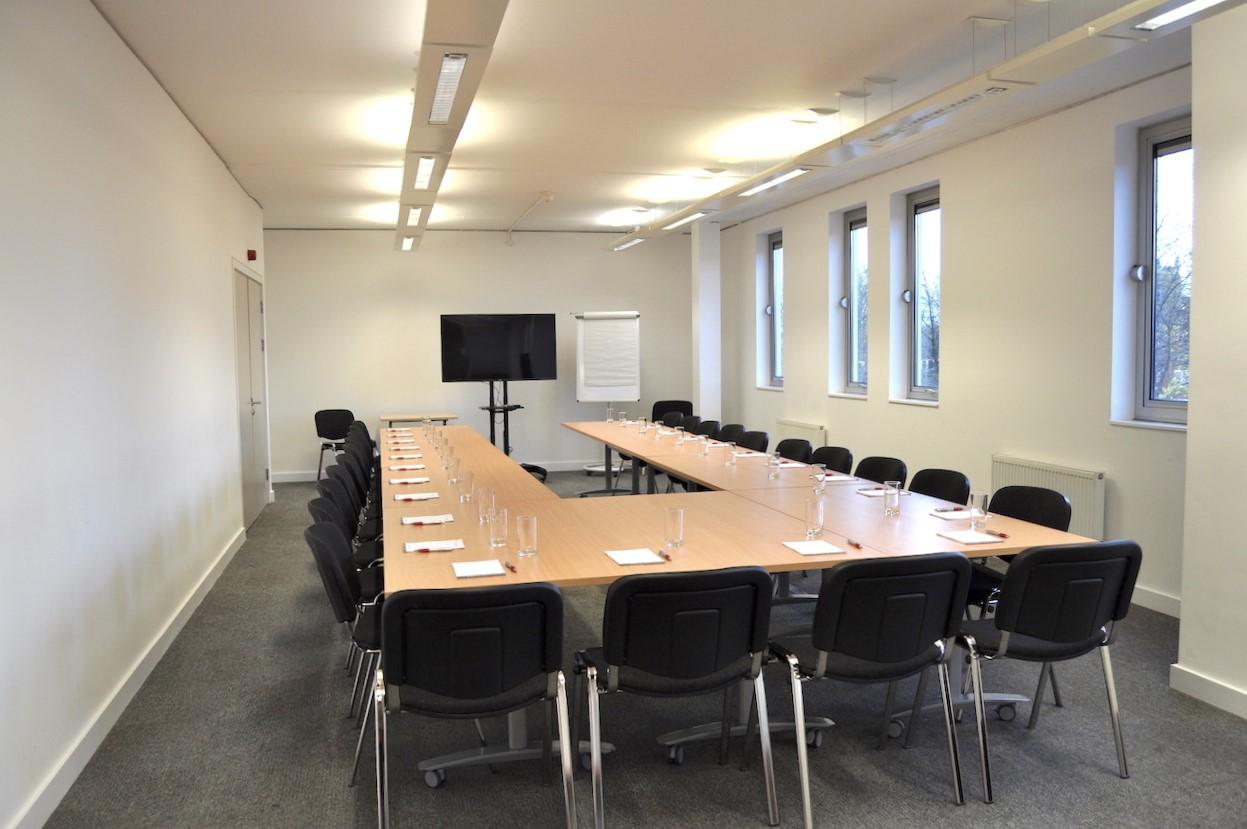 A conference centre meeting room with U-shaped tables, black chairs, and large windows at Signing Tree Venue.