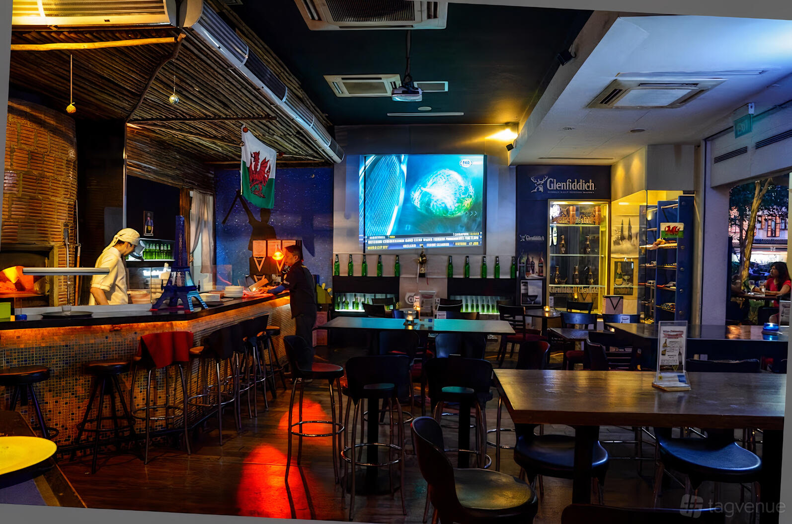 An event space with a long mosaic-tiled bar, bar stools, high tables, and a large wall screen at Hannibal.