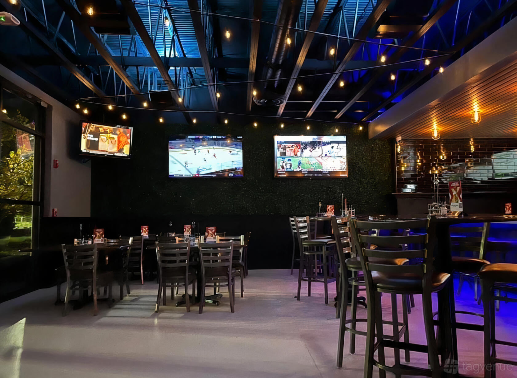 A sports bar with wall-mounted TVs, high tables, string lights, and a visible bar counter at Parlay Golf Sports Bar.