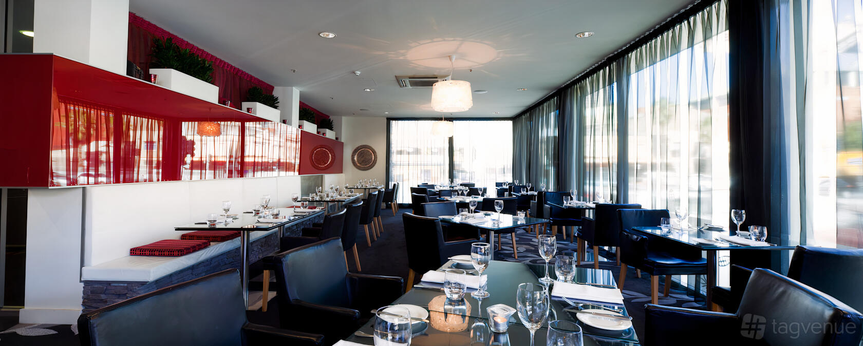 A hotel restaurant with floor-to-ceiling windows, sheer curtains, and tables set with glassware at Adelaide Rockford Hotel.