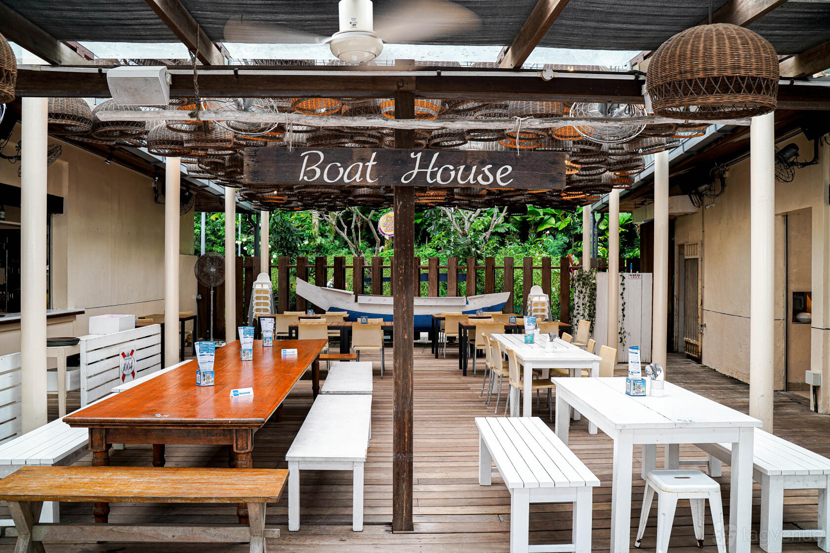 An outdoor dining area with wooden decking, a mix of communal and white picnic tables, and a wooden sign at Coastes.