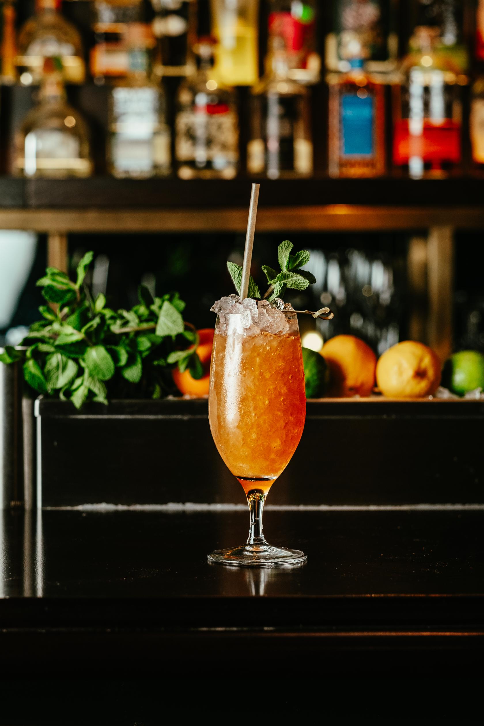 A cocktail bar featuring a tall glass of iced drink with mint garnish and fresh fruit on display at LOCKES Bar Covent Garden.