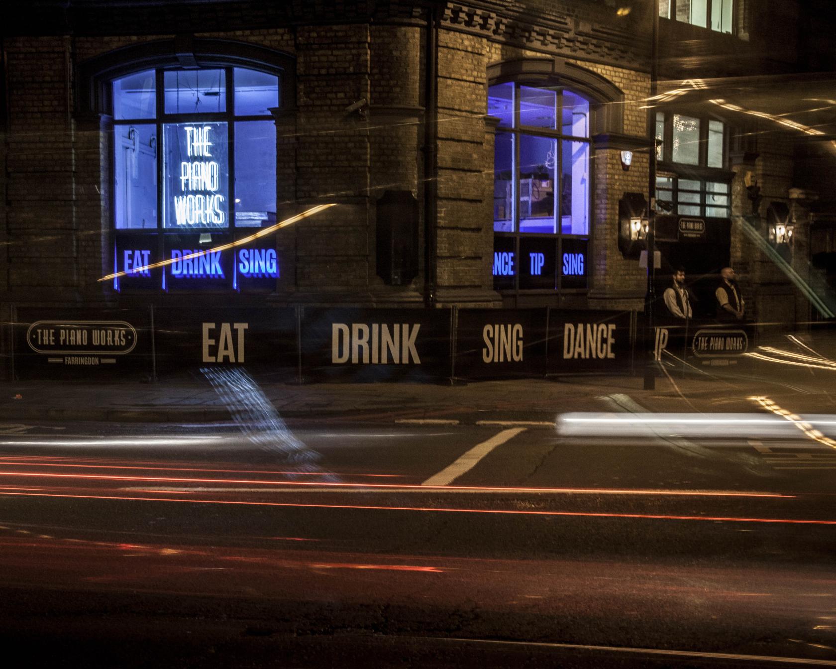 A nightclub with large arched windows, blue neon signage, and brick exterior at The Piano Works Farringdon.