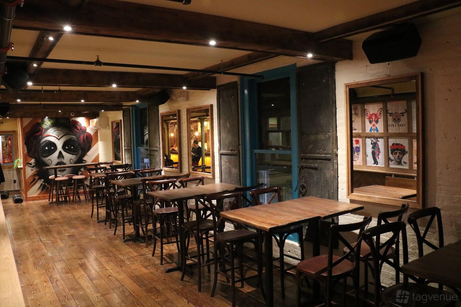 A bar space with wooden floors, exposed ceiling beams, colorful wall art, and large windows at Toro Loco.