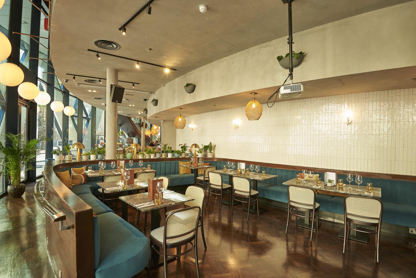 An event space in a restaurant with blue velvet banquettes, wooden tables, and globe pendant lights at The Sterling.