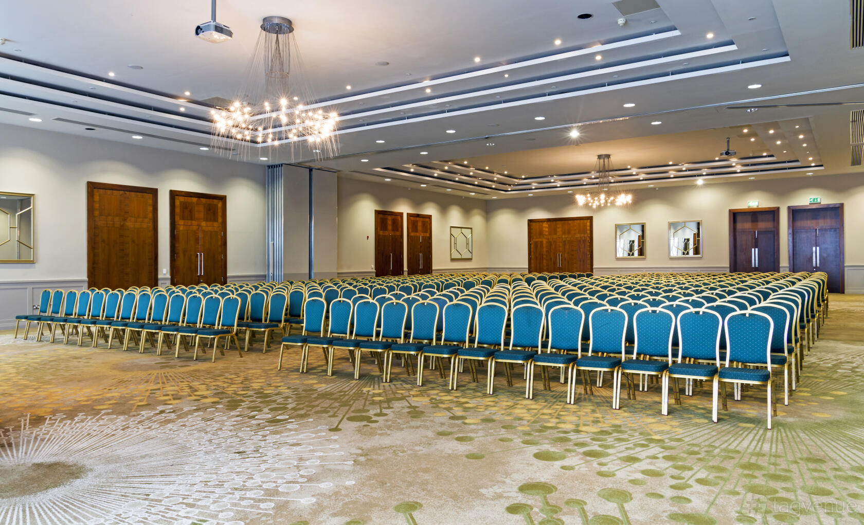 An auditorium with rows of blue chairs, chandeliers, and patterned carpet at CityNorth Hotel & Conference Centre.