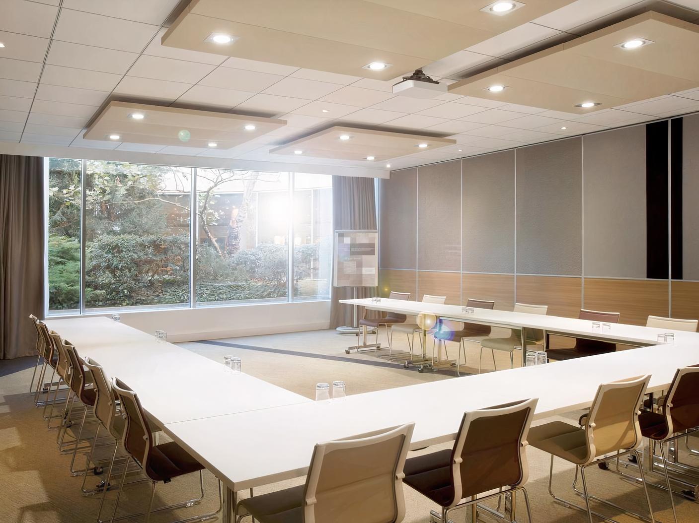 A meeting room with large floor-to-ceiling windows, natural light, and U-shaped tables at Novotel Manchester West.