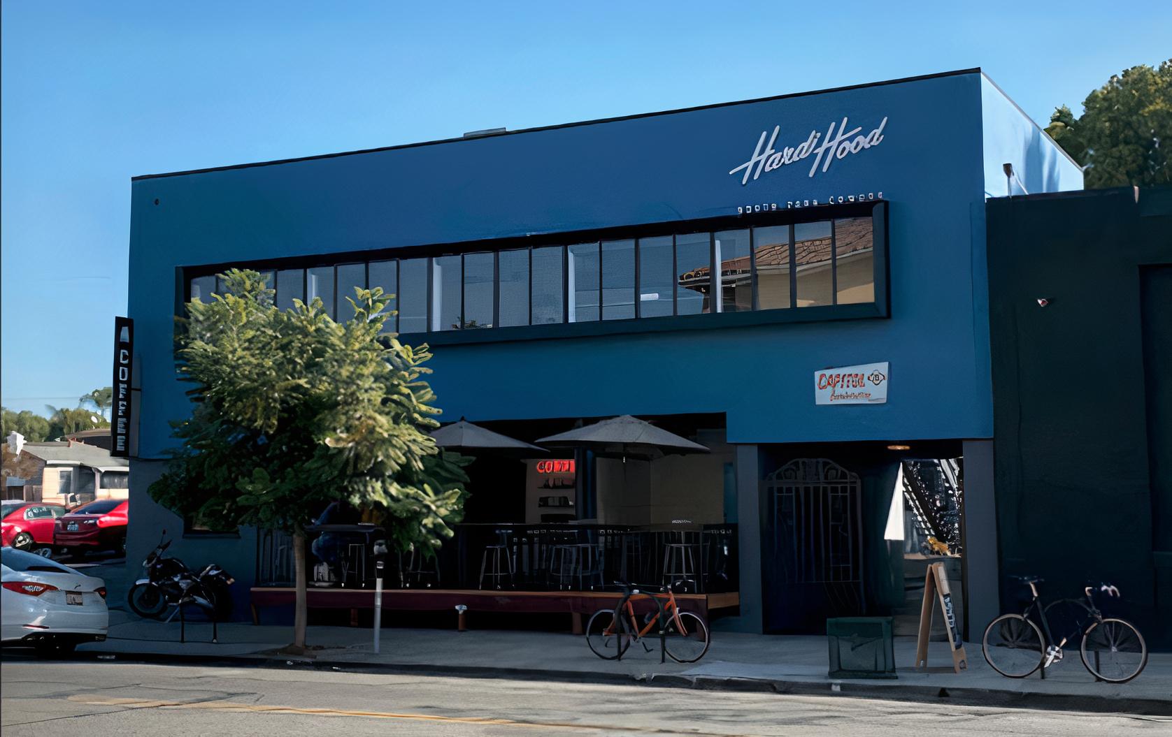 A coworking space with a blue facade, large windows, and an outdoor patio with umbrellas at Hardihood Cowork - North Park, San Diego.
