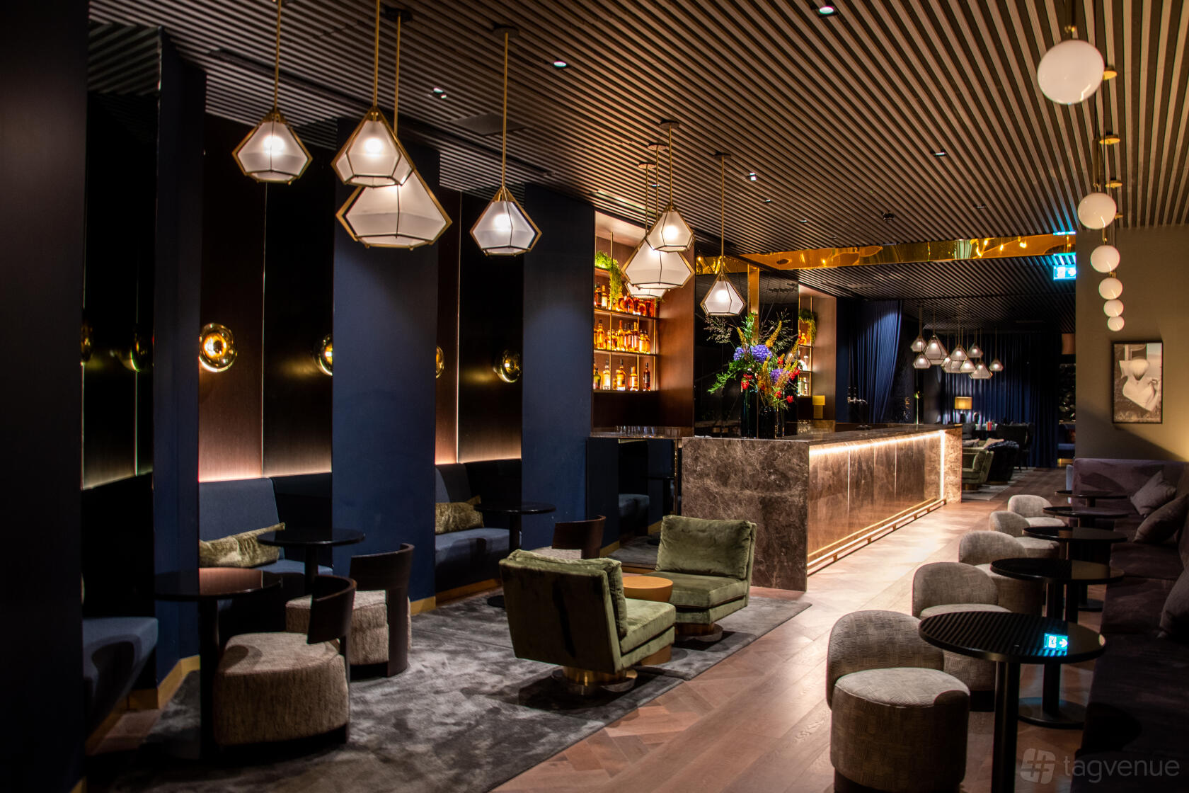 An event space with velvet lounge chairs, a marble bar, and pendant lighting at AMANO Hotel Covent Garden