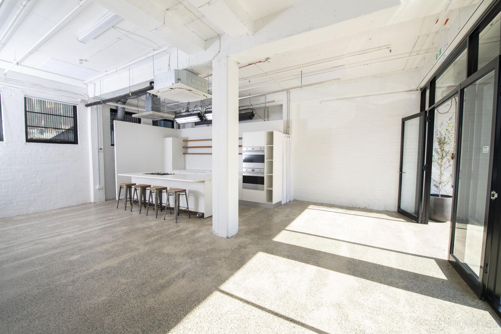 A photo studio with polished concrete floors, white walls, large windows, and a kitchen setup at Cutaway Studio.