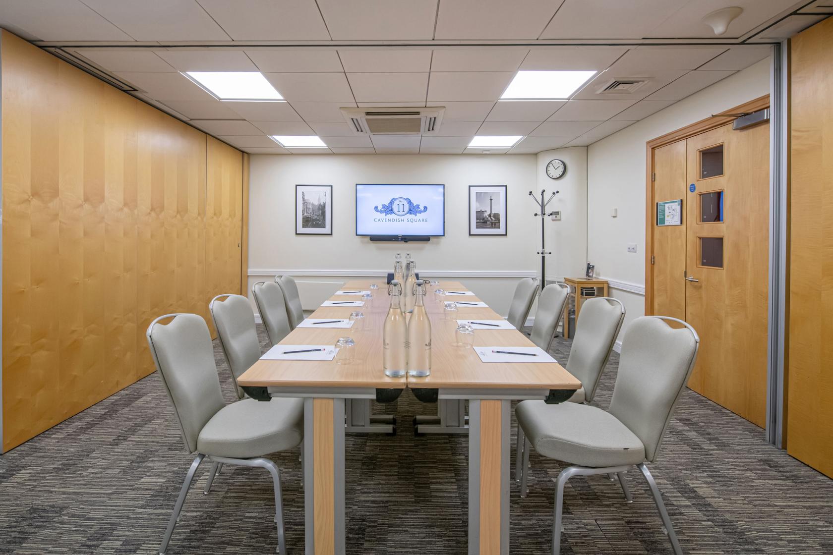 A meeting room with rectangular tables, white chairs, notepads, and a wall-mounted screen at No.11 Cavendish Square.