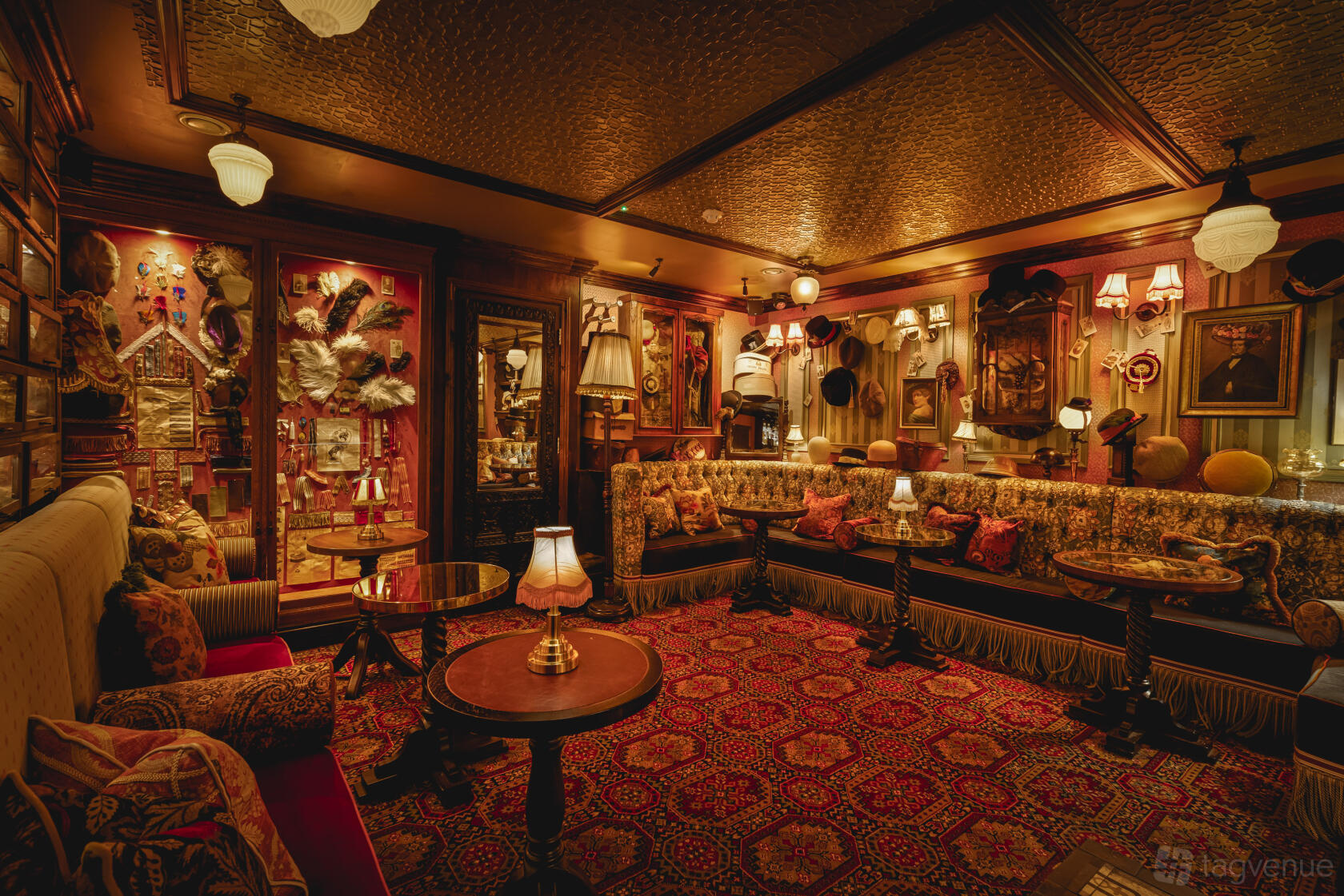 An event space in a pub with vintage patterned sofas, ornate lamps, and a wall display of hats at Mr Fogg's Hat Tavern and Gin Club.