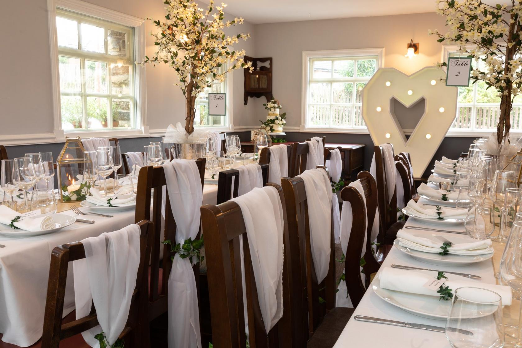 An event space with rectangular tables, white draped chairs, and lighted heart decor at The Lawrence Hotel.