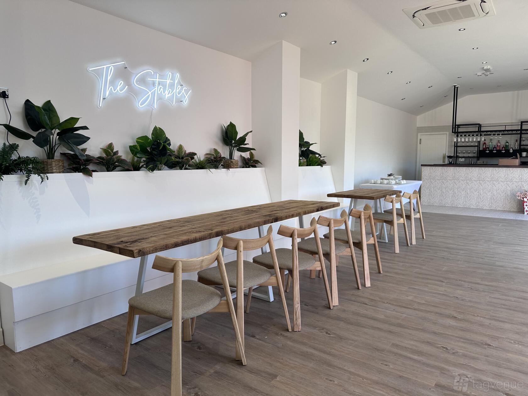 An event space in a pub with wooden tables, light wood chairs, potted plants, and a neon sign at Ye Olde Bridge Inn.