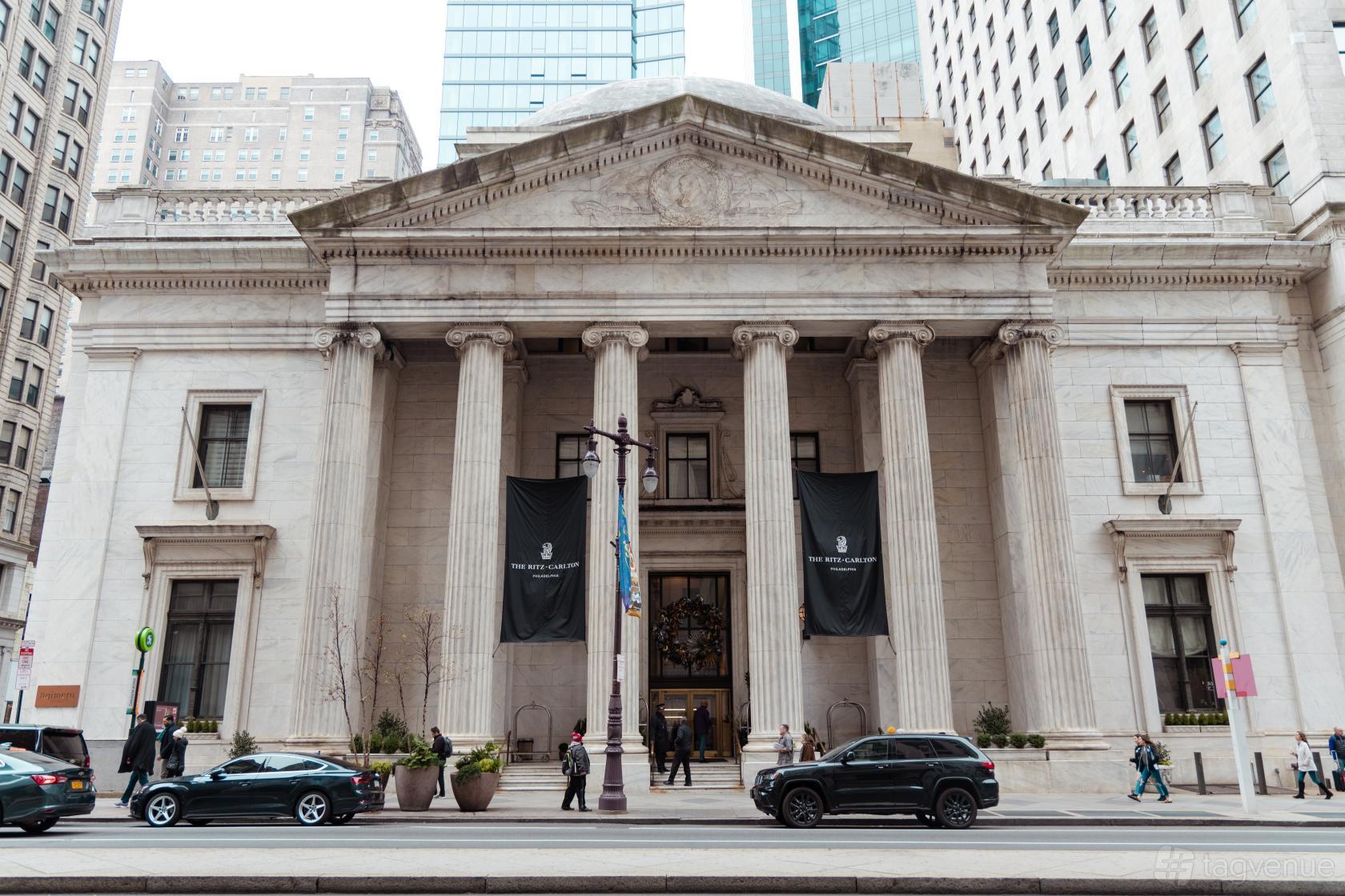 A restaurant with a grand neoclassical façade, tall stone columns, and large entrance banners at Aqimero.