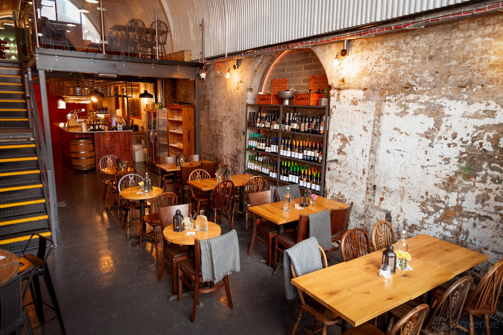 A bar with exposed brick walls, arched ceilings, wooden tables, and a wine bottle display at Pedro's Wine Bar.