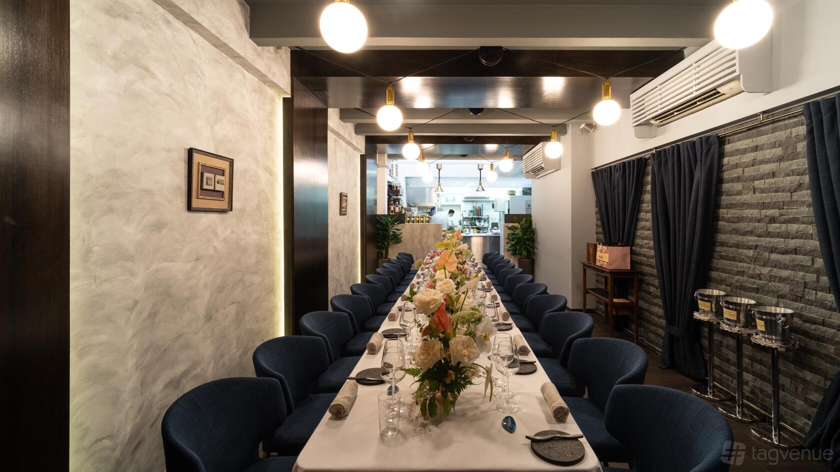 A dining room with a long table set with floral centerpieces and navy chairs under modern pendant lights at Restaurant JAG.
