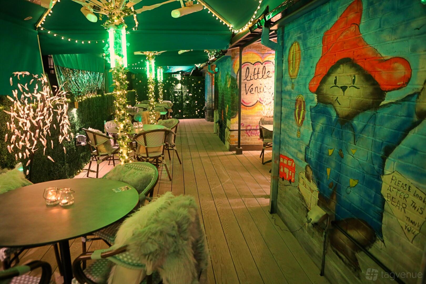 A hotel terrace with colorful mural walls, string lights, and bistro tables at Hotel Indigo London Paddington.