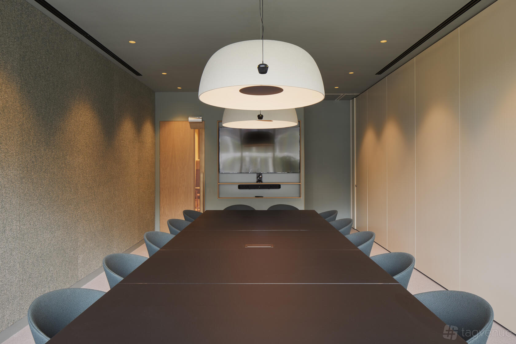 A meeting room with a long black table, modern chairs, pendant lighting, and a wall-mounted screen at Storey Club Broadgate.