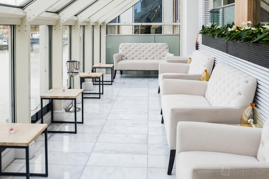 A restaurant lounge with tufted cream sofas, small wooden tables, and floor-to-ceiling windows at Bella Cosa Restaurant.