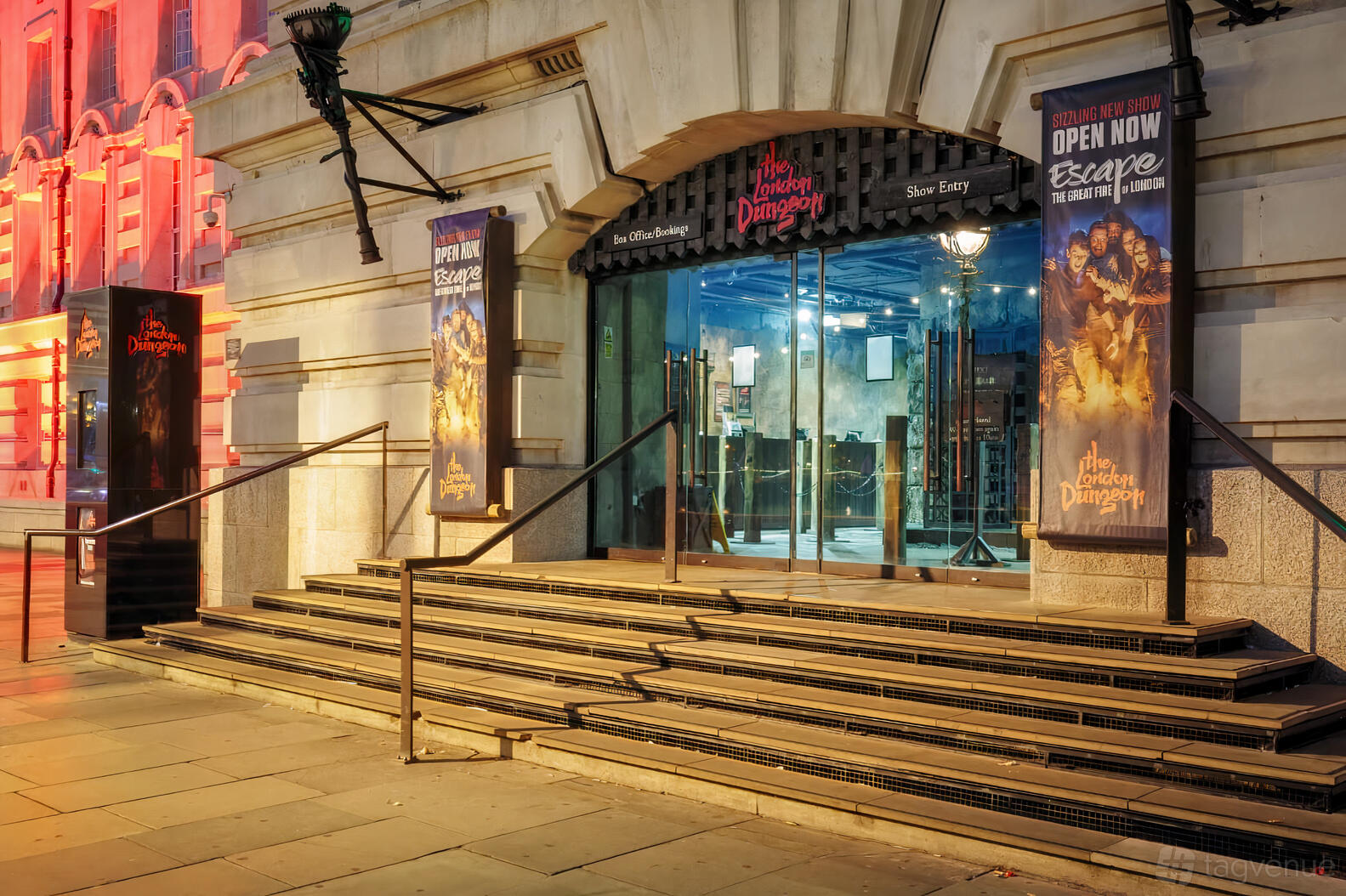An entrance to a pub with stone steps, arched glass doors, and themed signage at London Dungeon.