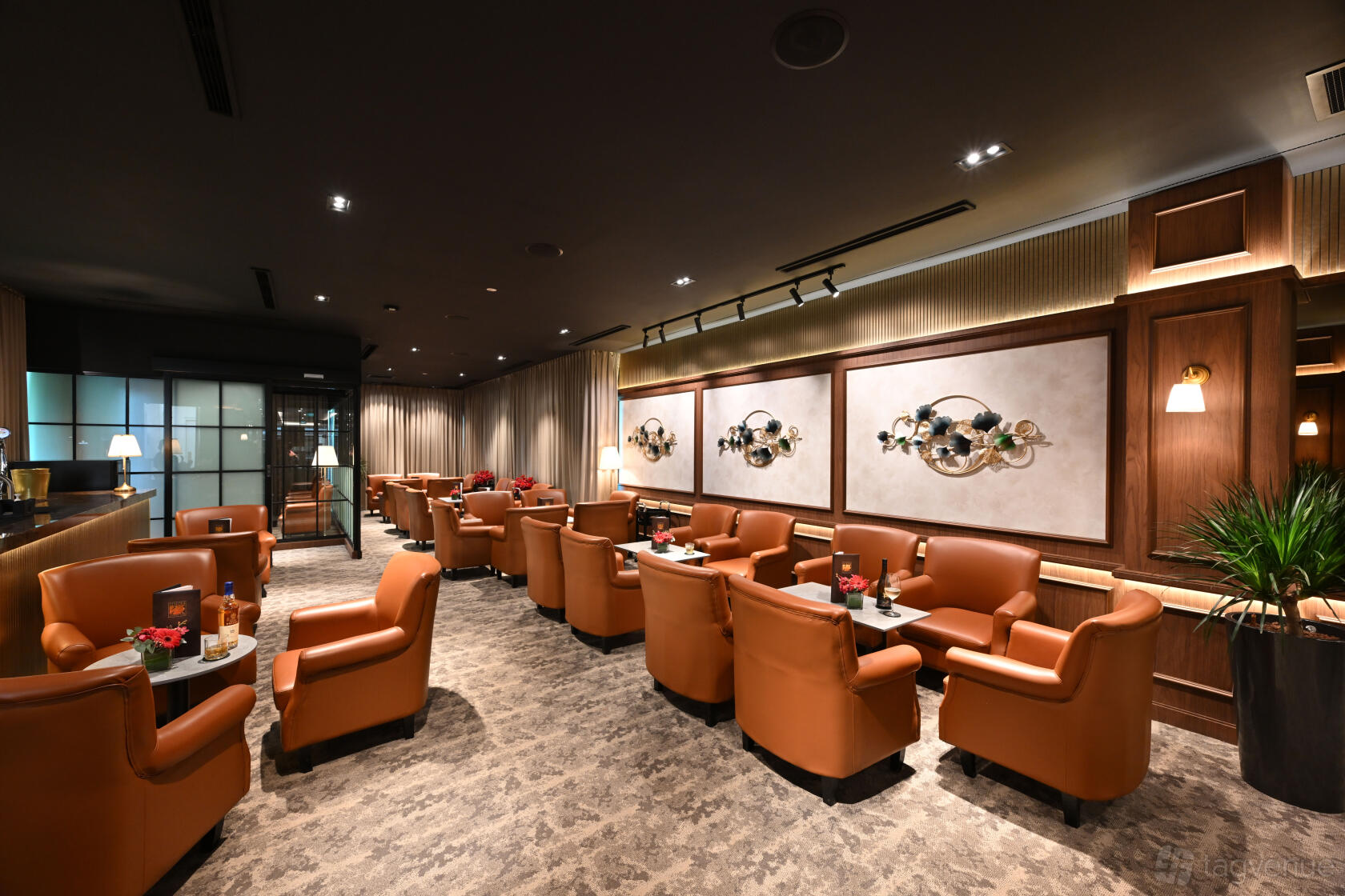 A lounge with leather armchairs, patterned carpet, wall art, and warm lighting at Seletar Country Club.
