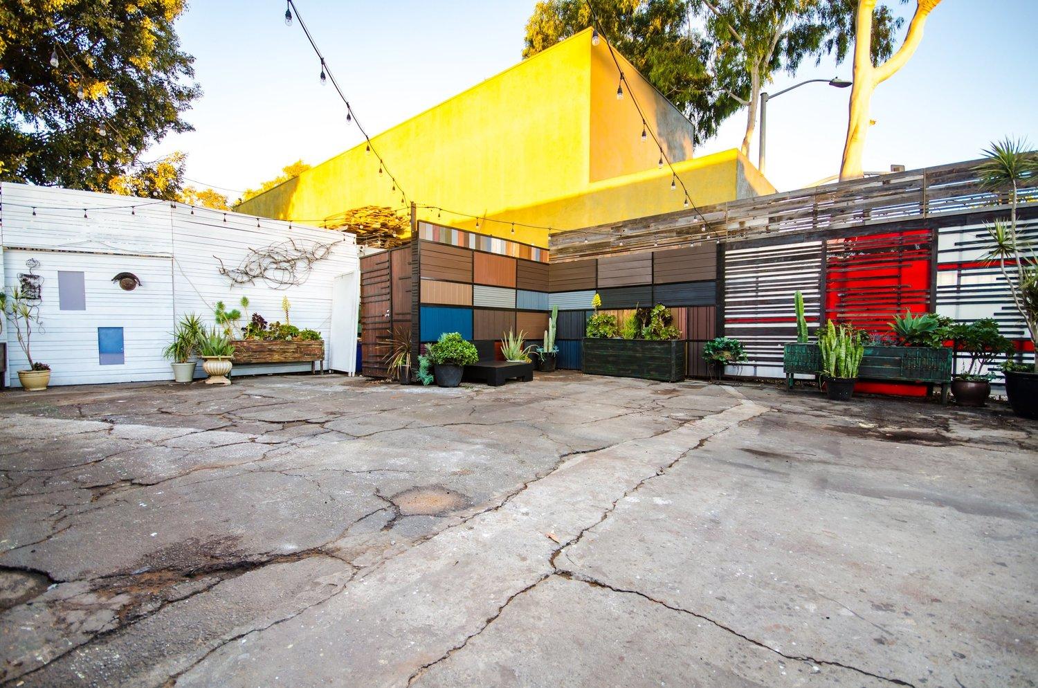 An outdoor event venue with colorful geometric wall panels, string lights, and potted plants at Mid-City Arthouse.