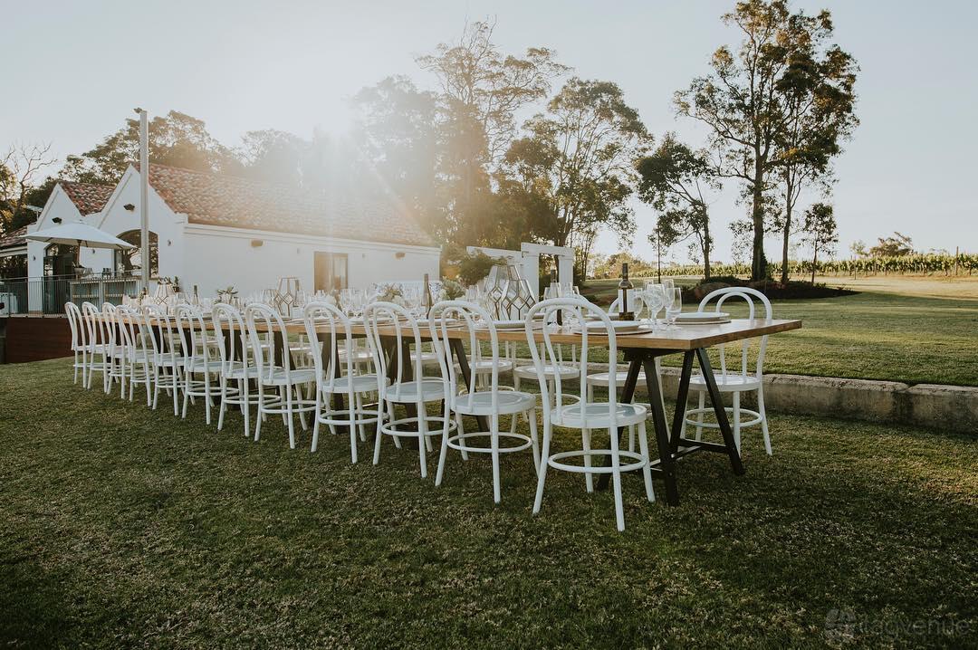 A country house lawn with long banquet-style table and white chairs set for dining at Credaro Wines.