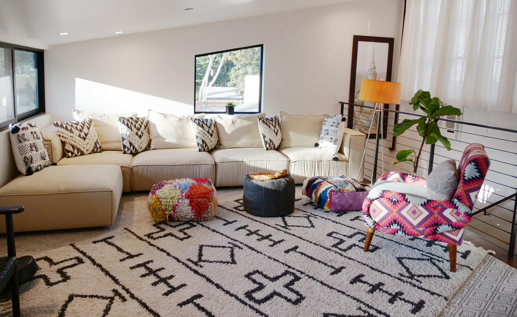 A loft with a large beige sectional sofa, geometric rug, patterned armchair, and bright natural lighting at Boho Chic Loft House.