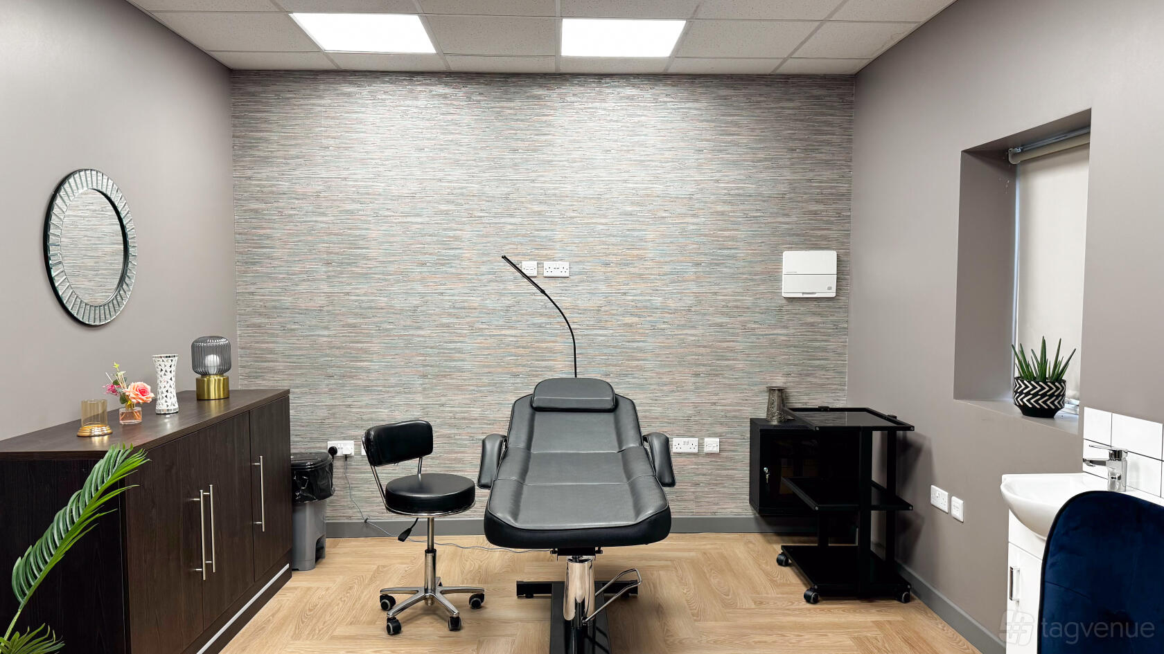 A therapy room with a reclining treatment chair, adjustable stool, and textured accent wall at Collaborative One - Flexible Spaces.