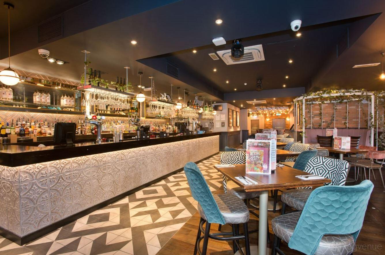A cocktail bar with a patterned tile floor, long illuminated bar, and velvet chairs at Slug & Lettuce, Colchester.