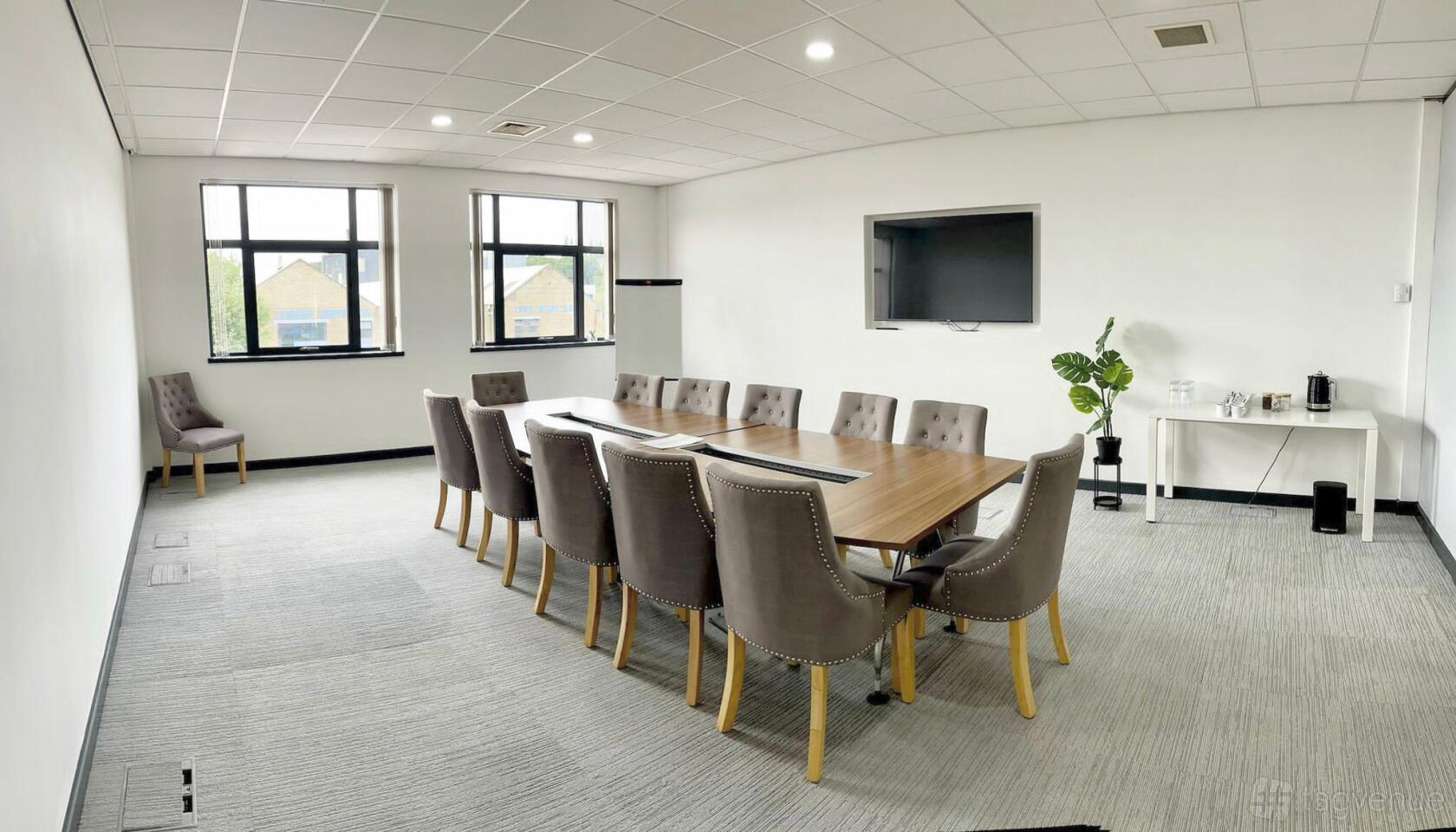 A meeting room with a long wooden table, upholstered chairs, wall-mounted screen, and windows at Lawrence House - Hub26.