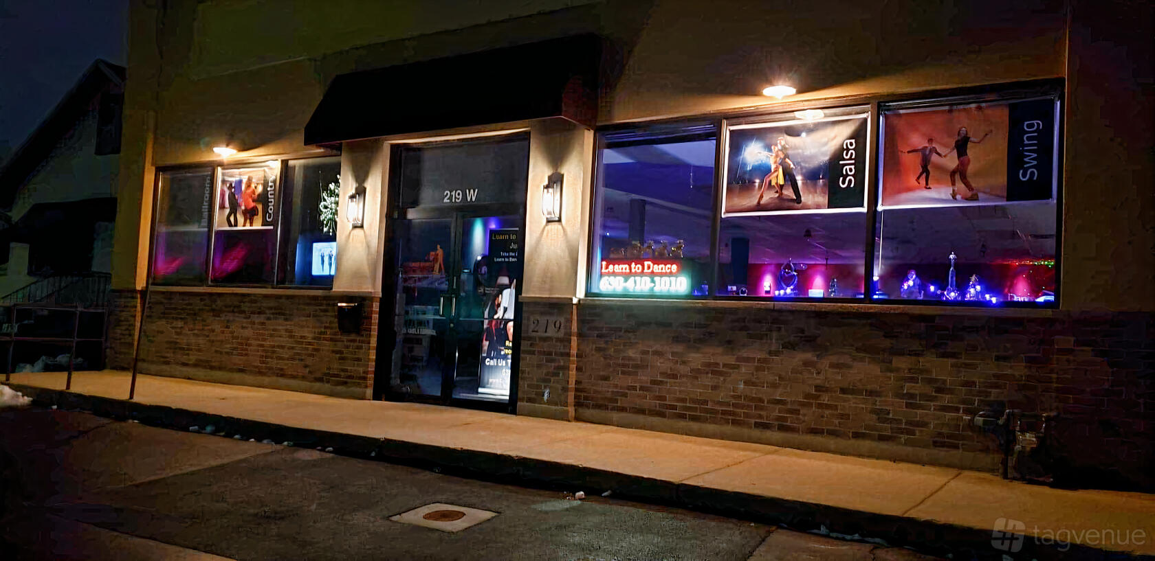 A versatile event space with large windows displaying dance posters and neon signage at Mystic Vines Comedy & Community Center.
