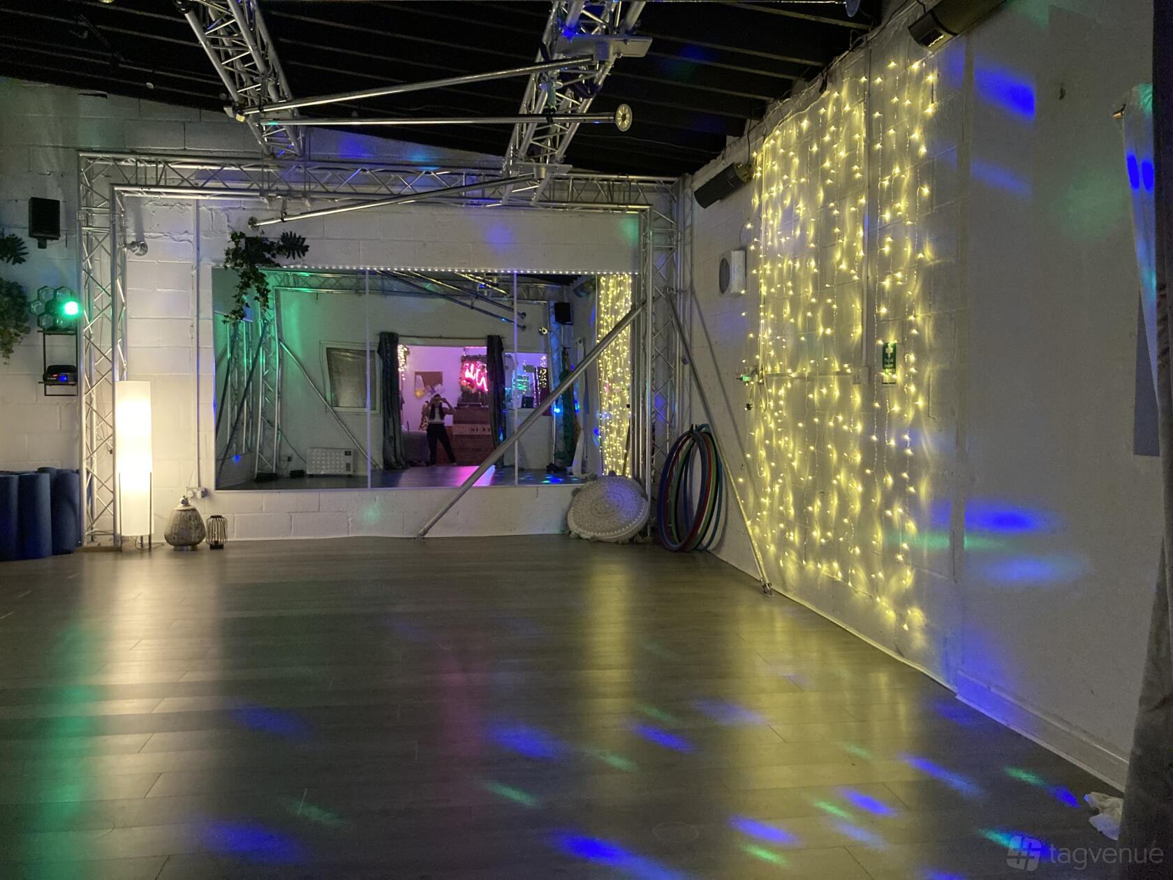 An event space in a fitness studio with a mirrored wall, string lights, wooden flooring, and hula hoops at Wild Workouts.