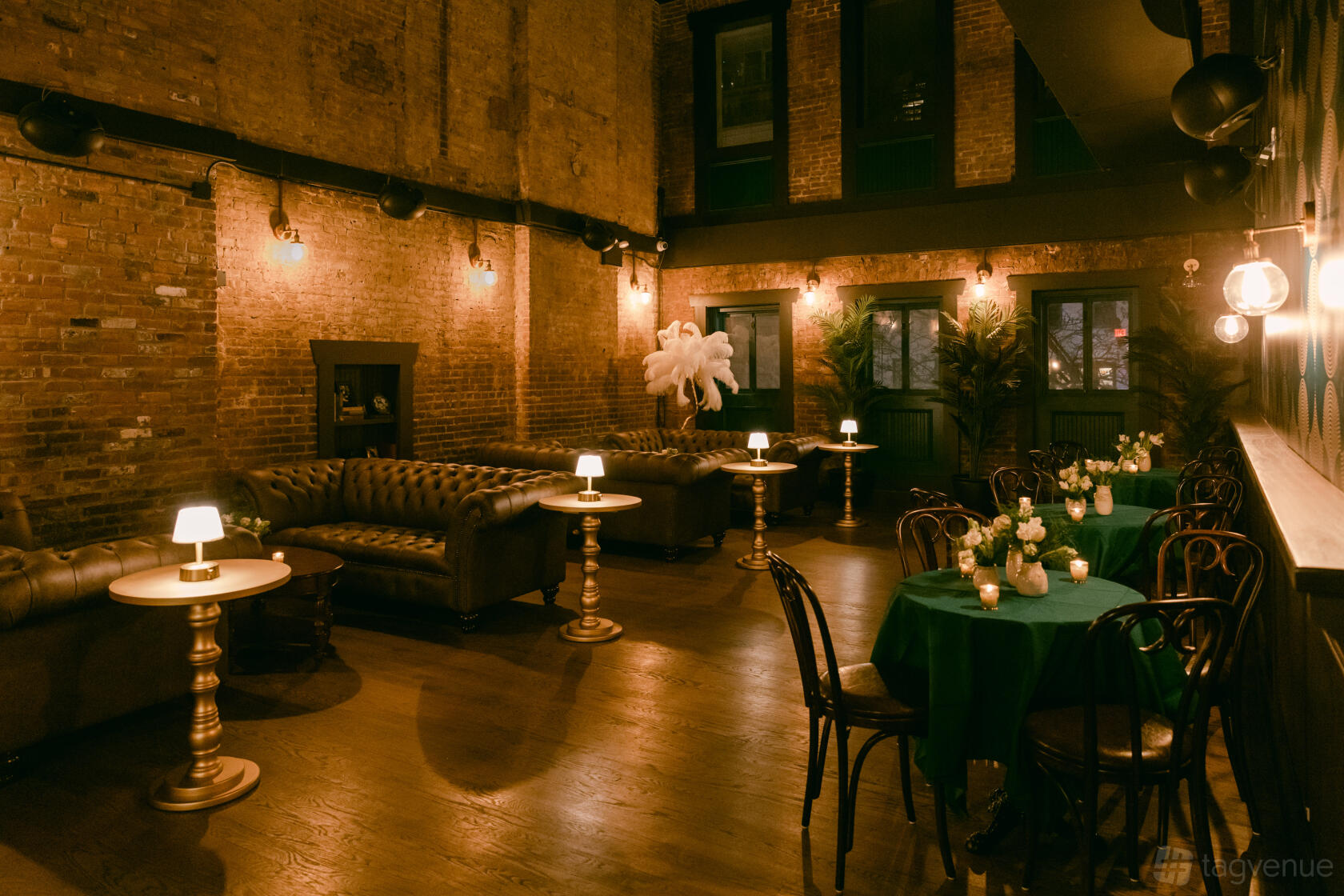 A restaurant with exposed brick walls, tufted leather sofas, and round tables with small lamps at Madam Mikette’s.