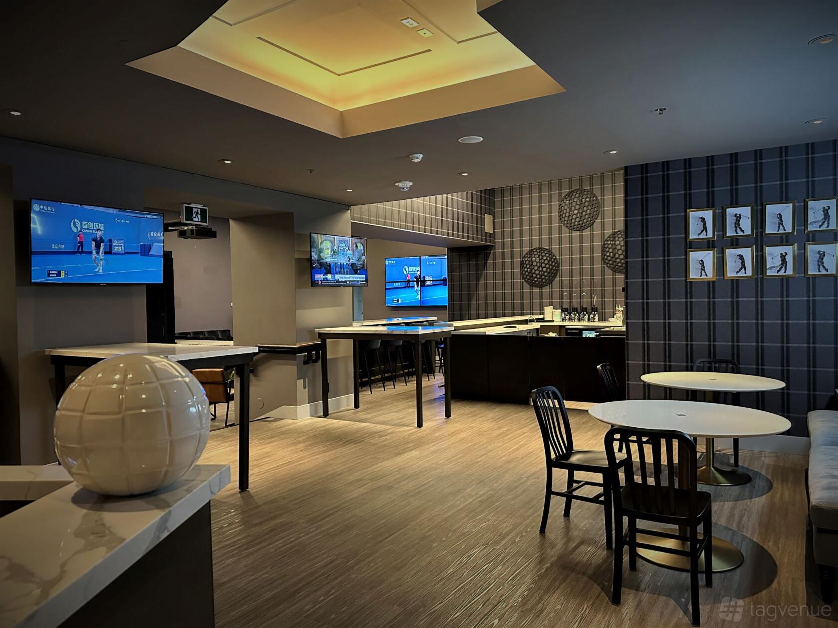A bar with golf simulator screens, high-top tables, and a patterned accent wall at PAR BAR Topgolf Swing Suite.