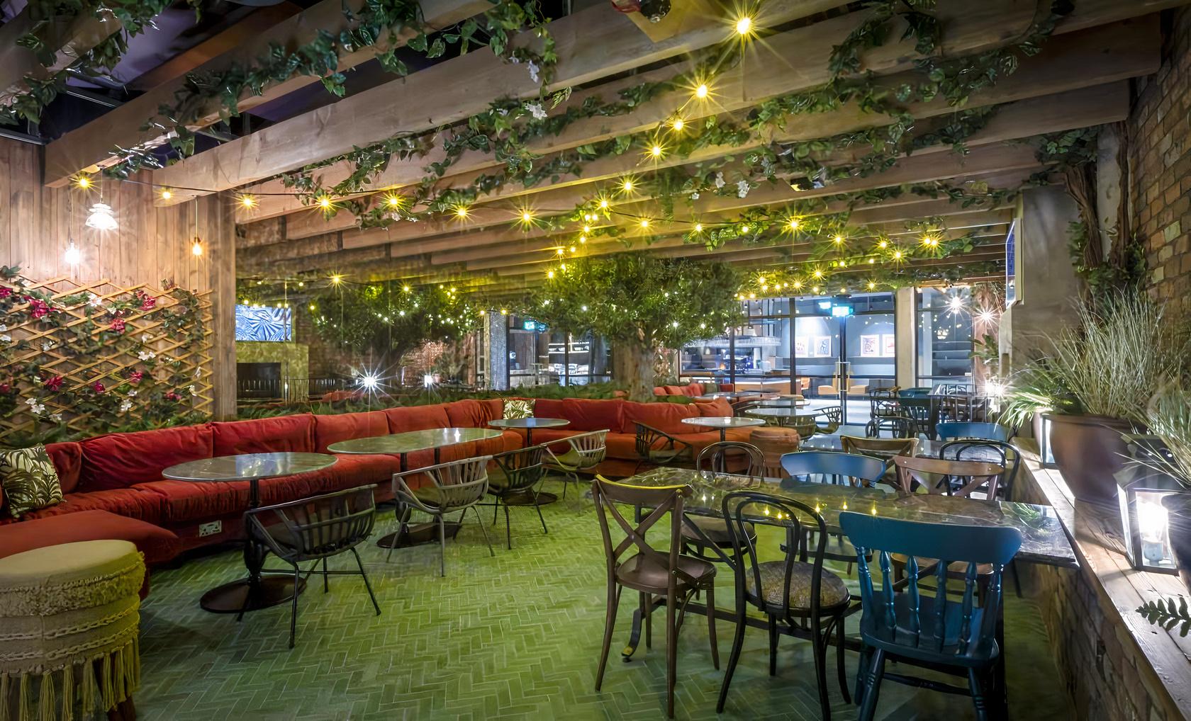 An event space with greenery, string lights, wooden beams, and mixed seating at Marlin Hotel.