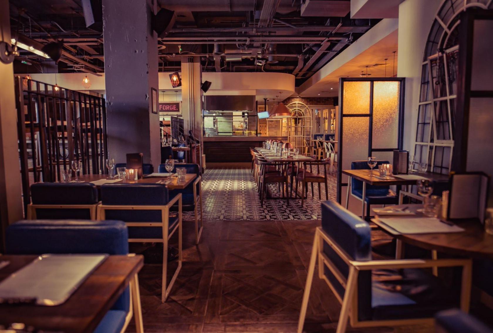 An event space with candlelit tables, blue chairs, wooden floors, and patterned tiles at Forge.