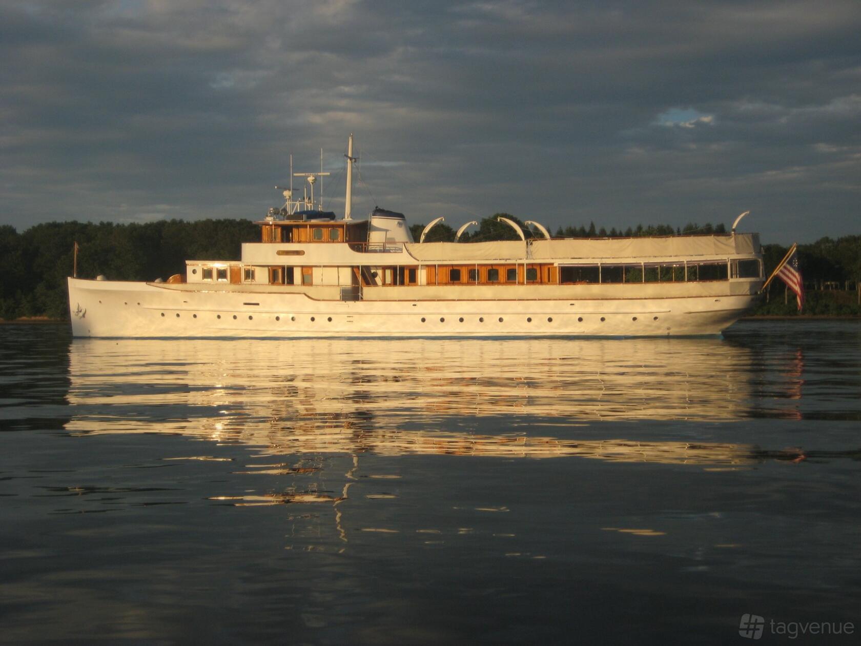 A classic yacht with wooden trim, open upper deck, and American flag on the water at Mariner III.