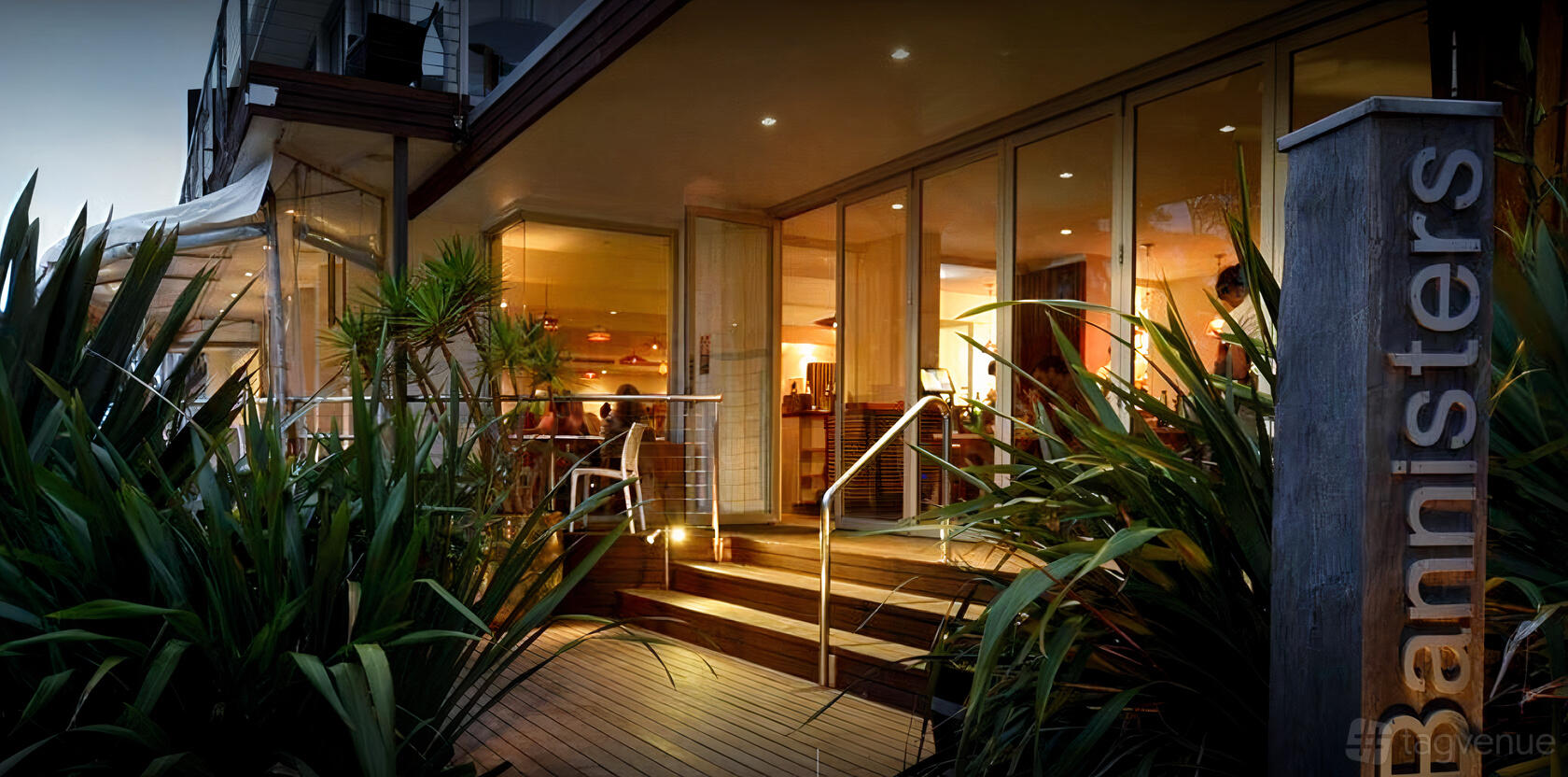 A versatile event space with glass walls and warm indoor lighting, visible from a deck with greenery at Bannisters by the Sea.