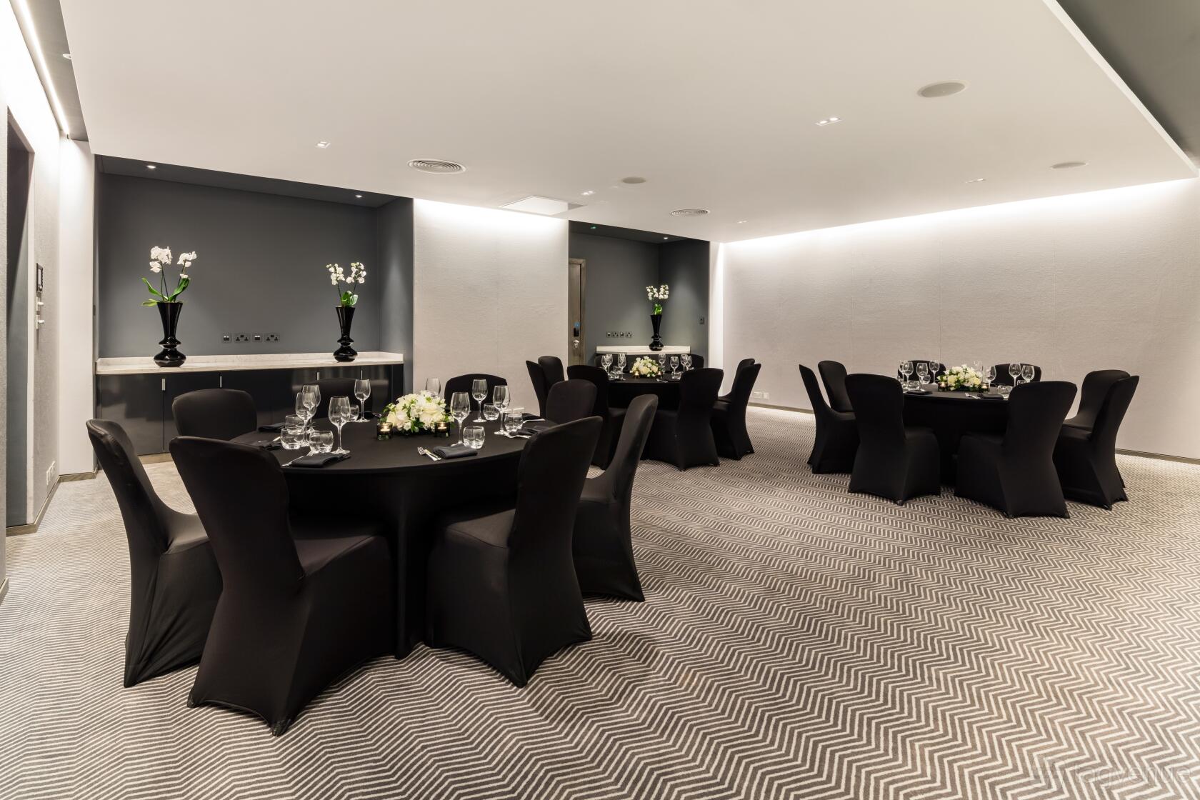 An event space with round tables covered in black linens, floral centerpieces, and patterned carpet at Radisson Blu Hotel, London Mercer Street.
