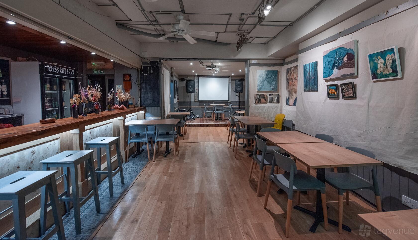 A hotel bar with wooden tables, contemporary chairs, a long counter, and paintings on the walls at 72 QT Guest House London.
