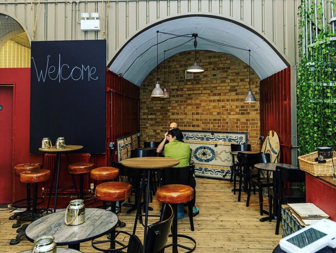 A bar with exposed brick walls, hanging pendant lights, and round wooden tables at Maltby Street Wine House.