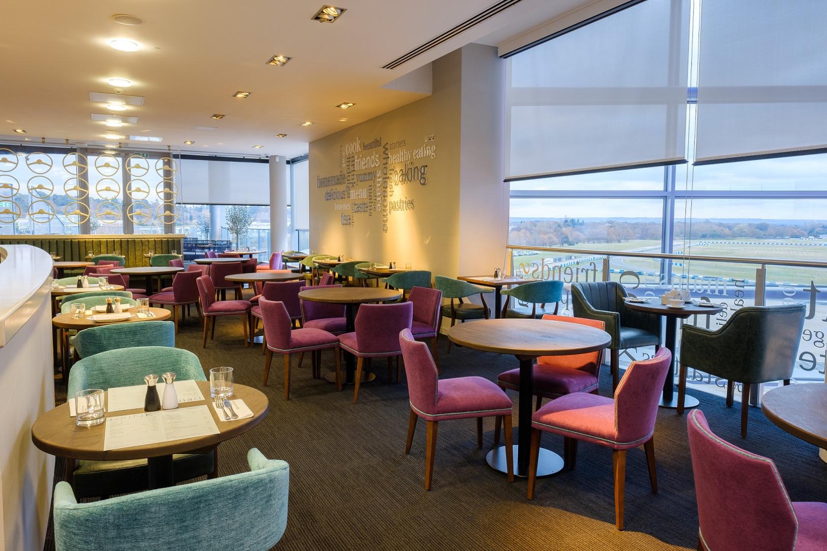 An event space with colorful velvet chairs, round wooden tables, and floor-to-ceiling windows at Mercedes-Benz World.