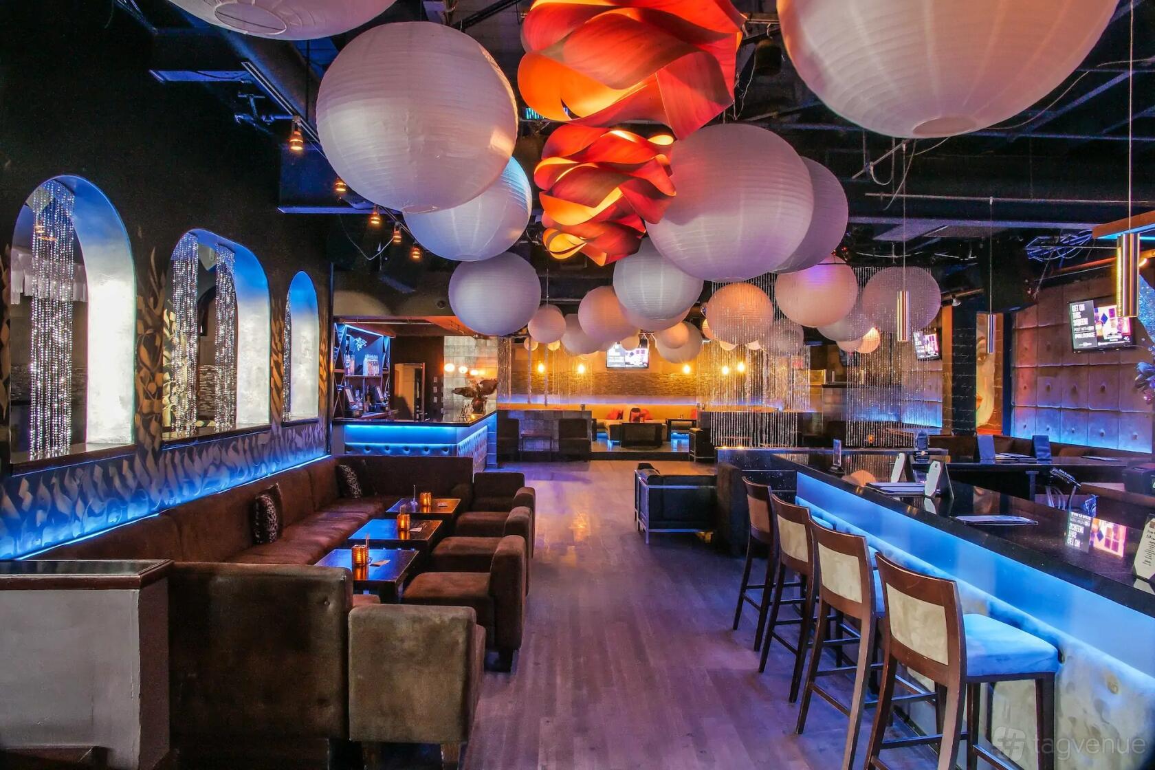 An event space in a bar with glowing blue accent lighting, paper lanterns, lounge seating, and a long bar at 46 Lounge.