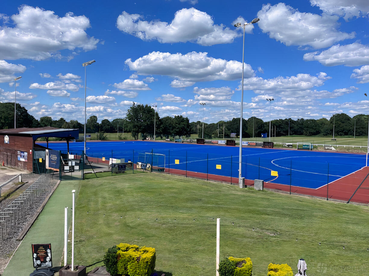 An outdoor sports field with a blue synthetic hockey pitch, red running track, and floodlights at Old Cranleighan Sports Club.
